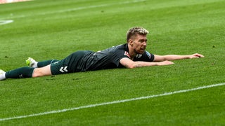 Werder-Spieler Mitchell Weiser liegt frustriert platt bäuchlings auf dem Rasen.