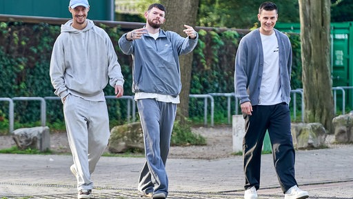 Die Werder-Profis Marco Friedl, Oliver Burke und Michael Zetterer in Straßenklamotten und lässiger Pose auf dem Weg vom Parkplatz zum Weser-Stadion.