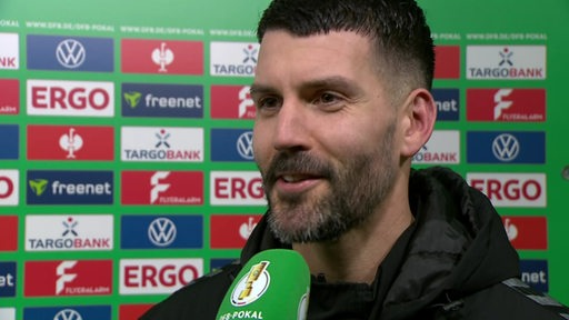 Werder-Torschütze Anthony Jung steht nach dem Pokalspiel gegen Darmstadt vor einer Werbewand beim Interview.