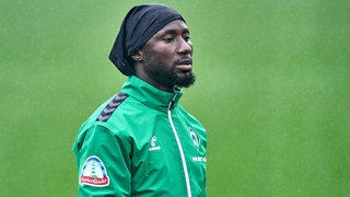 Werder-Profi Naby Keita mit einer schwarzen Mütze auf dem Kopf mit nachdenklicher Miene beim Training.