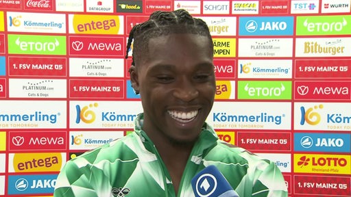 Werder-Torschütze Derrick Köhn strahlt nach dem Spiel in Mainz beim Interview vor einer Werbewand.