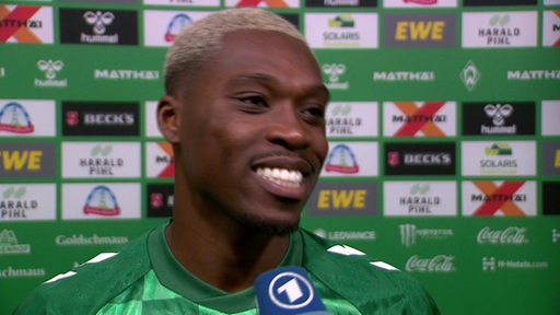 Werder-Profi Derrick Köhn steht lächelnd nach dem Spiel vor einer Werbewand beim Interview.