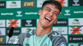 Werder-Fußballprofi Julian Malatini lacht ausgelassen bei einer Pressekonferenz.