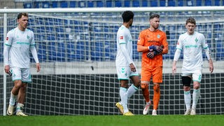 Werder-Spieler um Torwart Jiri Pavlenka und Jens Stage stehen mit hängenden Köpfen auf dem Platz.