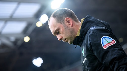 Werder-Trainer Ole Werner schaut vor dem Spiel im Freiburger Stadion nachdenklich nach unten.