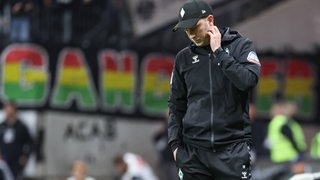 Werder-Trainer Ole Werner schaut nachdenklich am Spielfeldrand im Frankfurter Stadion auf den Boden.