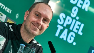 Werder-Trainer Ole Werner strahlt während einer Pressekonferenz.