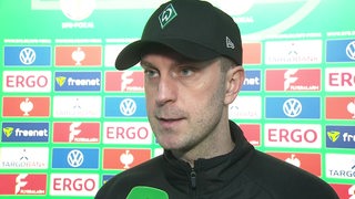 Werder-Trainer Ole Werner steht nach dem Pokal-Aus in Bielefeld vor einer Werbewand beim Interview.