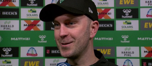 Werder-Trainer Ole Werner steht lächelnd nach dem Spiel vor einer Werbewand beim Interview.