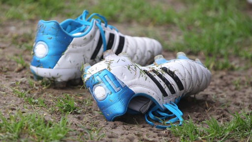 Dreckige Fußballschuhe in blau und weiß liegen auf dem Boden