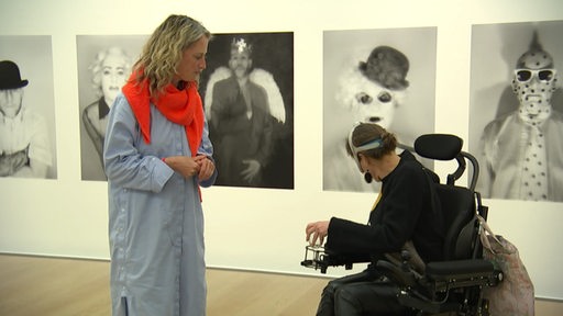 Zwei Personen in der Kunsthalle und eine sitzt von ihnen im Rollstuhl.
