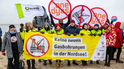 Menschen mit Banner protestieren am Strand gegen Gasbohrung