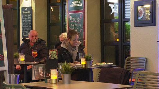 Mehrere Personen sitzten draußen an Tischen eines Restaurants.