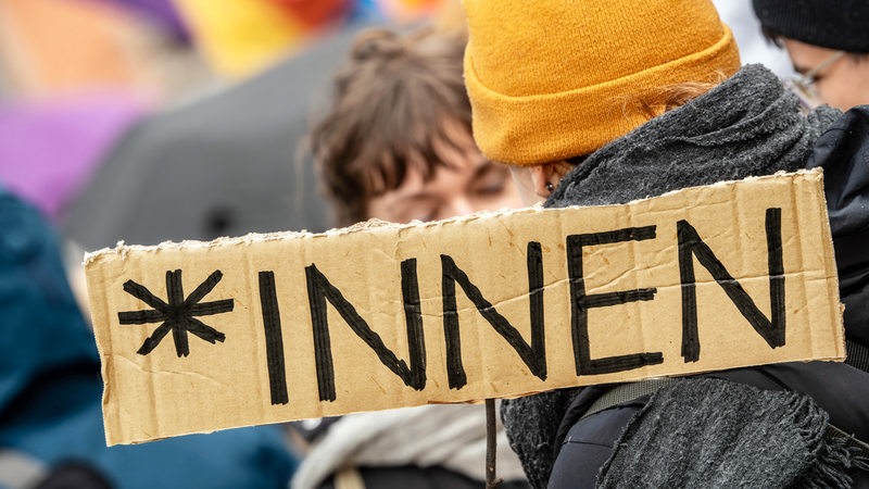 Auf einem Schild steht *innen, aufgenommen bei Demo gegen Söders Genderverbot. Im Hintergrund sind Demoteilnehmende zu sehen.