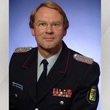 Ein blonder Mann in Uniform blickt in die Kamera.