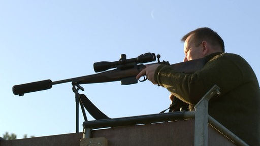 Ein Mann stützt ein Gewehr an seiner Schulter ab