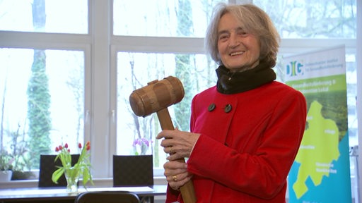 Barbara Stollberg lächelt und hält einen großen Hammer in den Händen.