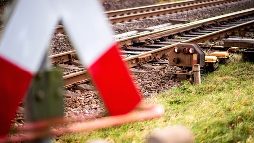 Im Vordergrund sieht man ein Andreaskreuz. Im Hintergrund Bahngleise.