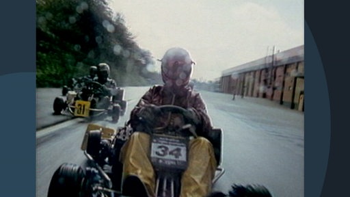 Mehrere Karts fahren über eine Rennstrecke, die Fahrer tragen Helme und Schutzkleidung.