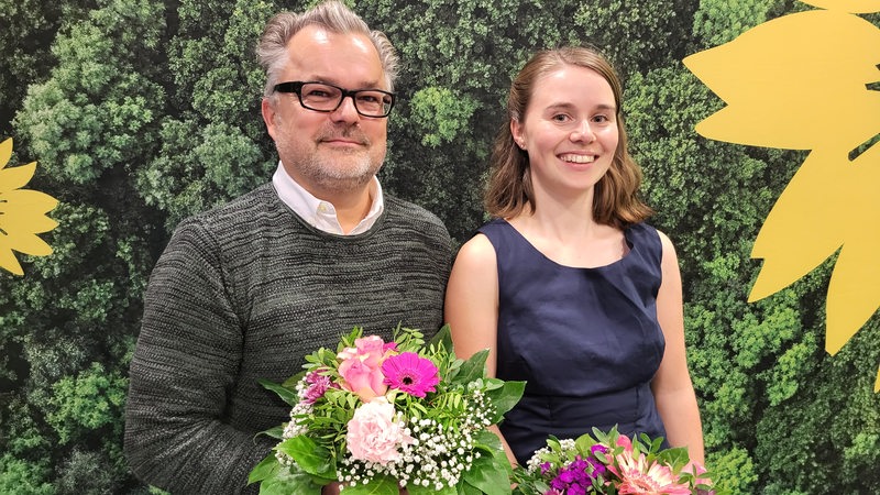 Ein Mann und eine Frau stehen vor einem grünen Hintergrund nebeneinander