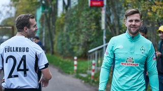 Ein Fan trägt neben dem Trainingsplatz ein Nationaltrikot mit Füllkrug-Flock- Niclas Füllkrug lächelt daneben.