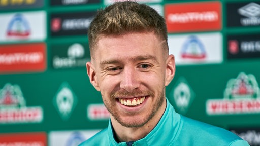 Werder-Profi Mitchell Weiser lächelt bei einer Pressekonferenz.