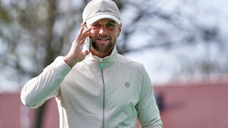 Werder-Stürmer Niclas Füllkrug auf dem Weg ins Weser-Stadion mit beiger Baseball-Kappe und Handy am Ohr lächelt in die Kamera.