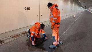 Bauarbeiter stehen in einem leeren Tunnel und arbeiten am Boden.