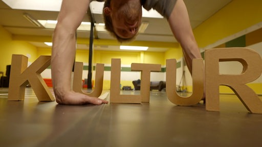 Ein Tänzer macht einen Handstand über einem Kultur Schriftzug