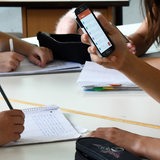 Ein Schüler hält im Unterricht ein Handy in den Händen.