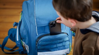 Ein Grundschüler packt ein Handy in seinen Ranzen.