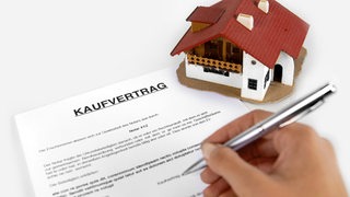 Eine Hand unterschreibt einen Kaufvertrag für ein Haus