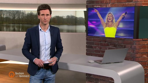 Moderator Janos Kereszti im Studio von buten un binnen. Auf dem Monitor im Hintergrund ein Bild von Helene Fischer.