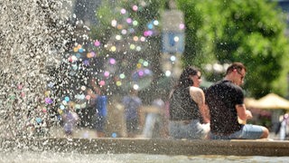 Menschen sitzen an einem Brunnen, die Sonne scheint