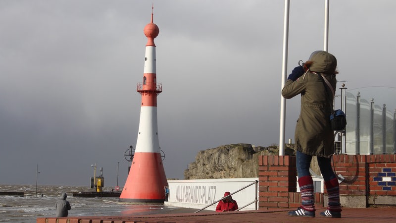 Eine Frau stemmt sich am Wasser gegen den Wind.