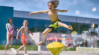 Kinder springen im Horner Freibad über Wasserspiele.