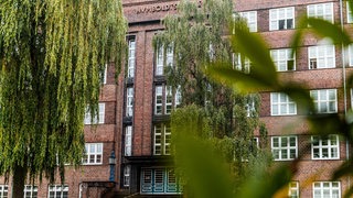 Blick auf ein rotes Backsteingebäude. Davor stehen Bäume.