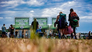 Junge Menschen laufen bepackt mit Rucksäcken auf das Hurricane-Festival-Gelände zu.