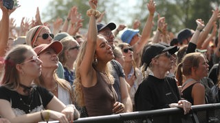 Menschen stehen vor einer Bühne und hören einem Konzert zu.