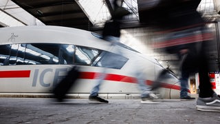 Reisende gehen an einem Bahnsteig an einem ICE der Deutschen Bahn vorbei