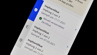 Auf einem Handy-Display sieht man drei Corona-Impfzertifikate