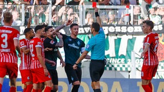 Der Schiedsrichter ist umringt von Freiburger und aufgeregten Werder-Spielern, als er Kapitän Marco Friedl die Rote Karte zeigt.