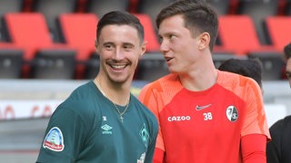 Werder-Kapitän Marco Friedl strahlt im Gespräch mit Landsmann Michael Gregoritsch beim Gespräch vor dem Spiel in Freiburg.