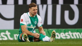 Werder-Stürmer Niclas Füllkrug sitzt auf dem Boden und zieht sich die Stutzen hoch.