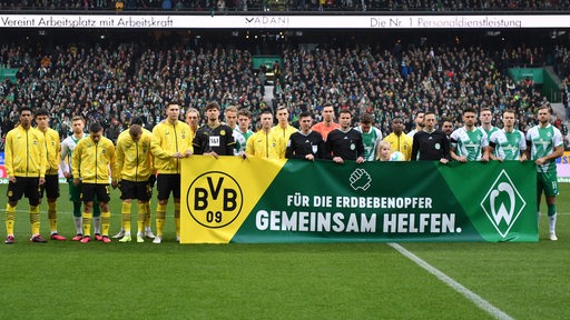 Die Spieler von Werder und Dortmund stellen sich vor dem Spiel hinter einem Banner mit der Aufschrift "Für die Erdbebenopfer – Gemeinsam helfen" auf.