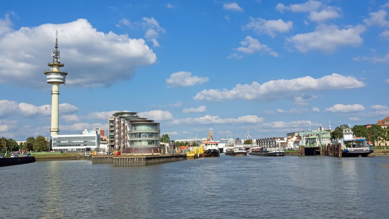 Vom Wasser aus ist das Ufermit Gebäuden und Schiffen zu sehen.