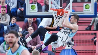 Eisbären-Profi Robert Oehle hält sich im Sprung am Ring des Basketballkorbes fest.