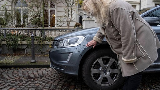 Eine Frau begutachtet einen Kratzer in ihrem Auto