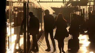 Bahnreisende Pendler steigen im morgendlichen Gegenlicht in einen Zug ein.