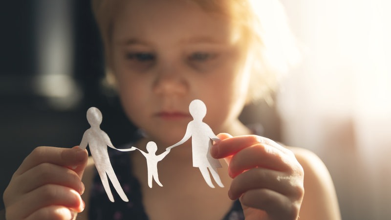 Kleines Mädchen mit gebastelter Papierfamilie in den Händen (Symbolbild)